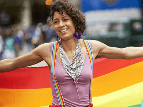A person smiling holding a rainbow flag behind her back