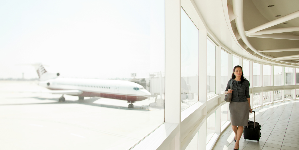 A woman walks through an airport pulling her luggage with airplane in the background.