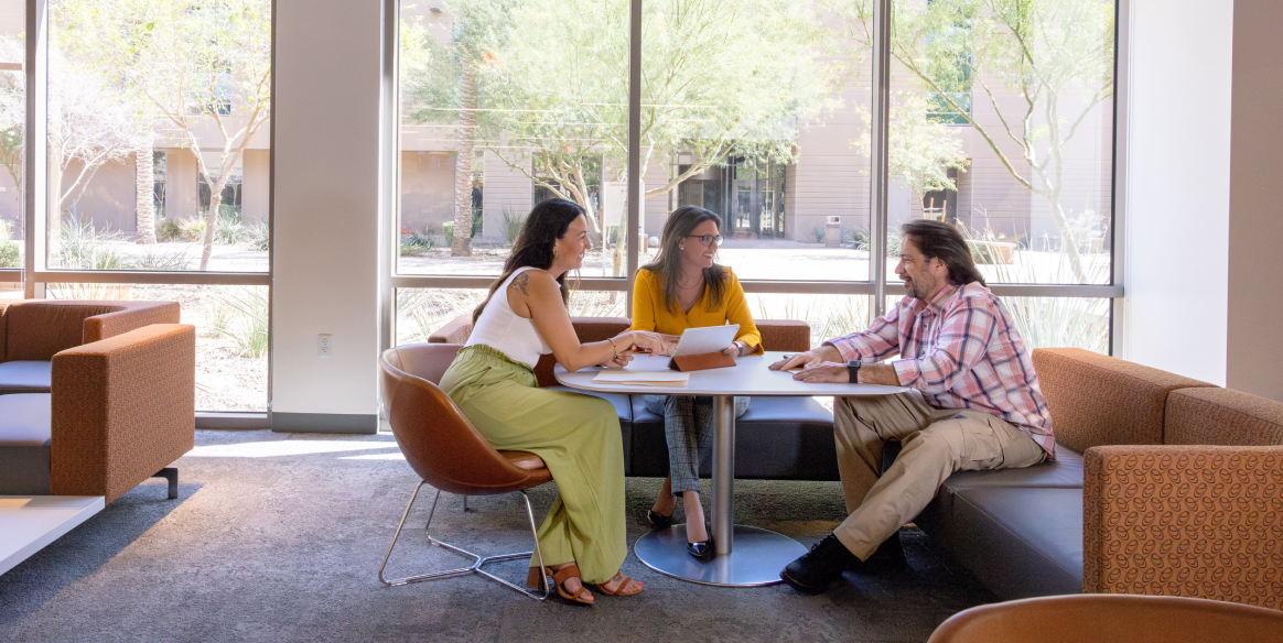 Three coworkers sit around a table in a sustainable work environment