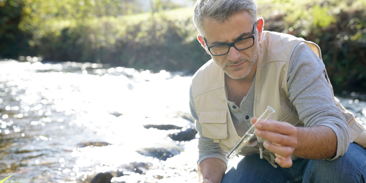 A person inspects a water sample from a river.