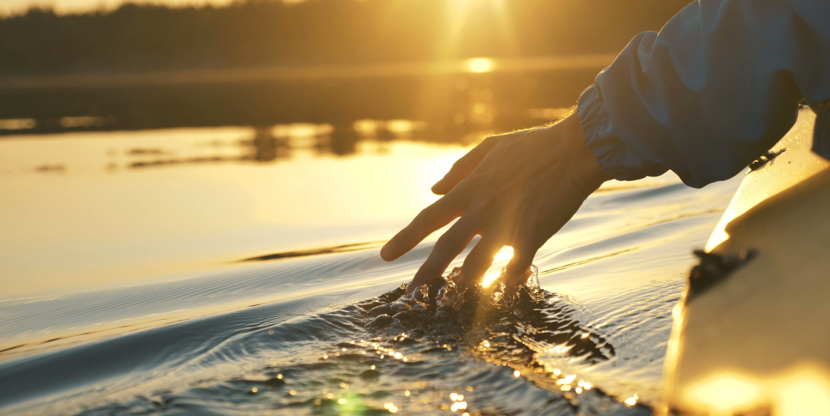 Man in a kayak on a lake running his hand through the water with the sunset in the background
