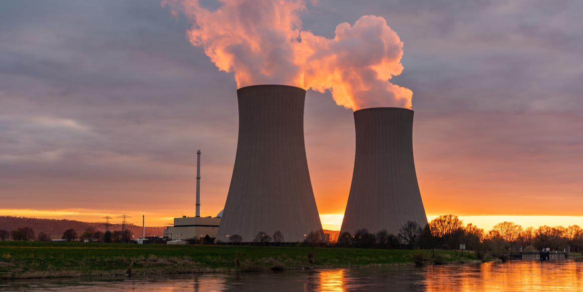 Water vapor is released from two nuclear power plant cooling towers beside a river at sunset.