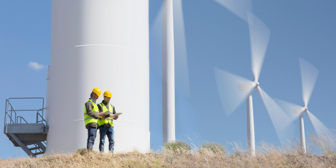 Two workers by wind turbines in rural landscape.