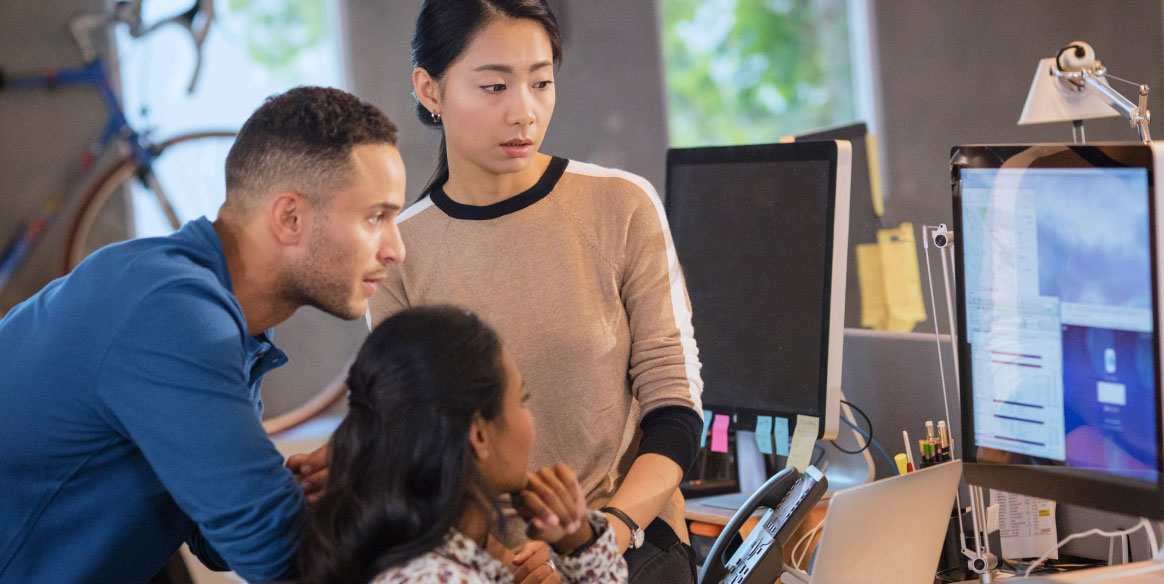 Three coworkers huddle around a computer in an office.